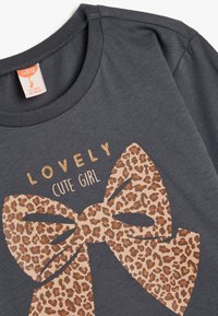 Szara bawełniana koszulka z dużą grafiką w kształcie bowu w leoparda z złotymi akcentami i napisem "Urocza Słodka Dziewczyna" powyżej.
