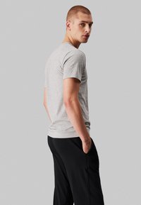 Gray short-sleeve t-shirt made of soft fabric, paired with black pants, shown from the side with a plain background.