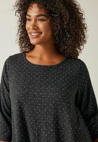 Schwarzes Oberteil mit Polka-Dots, dreiviertelärmlig und mit rundem Halsausschnitt. Weicher Stoff mit lockerem Schnitt. Verfügt über weiße gesprengte Muster.