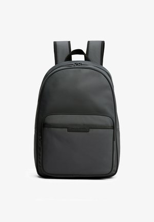 Zaino nero con spallacci imbottiti, tasca anteriore con cerniera e maniglia superiore, in piedi su uno sfondo bianco.