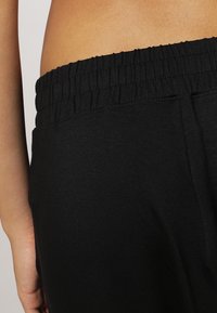 Cintura elastica nera dei pantaloni, caratterizzata da una texture arricciata. Il materiale sembra morbido, adatto per un abbigliamento casual o per il relax.