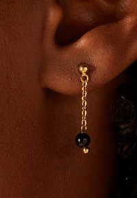 Boucles d'oreilles en chaîne dorée mettant en valeur une perle noire ronde et une petite boule dorée, arborant un design délicat avec une texture lisse.