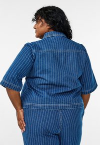 Camisa de mezclilla de manga corta, con tejido azul y rayas verticales blancas. Incluye un cuello y costuras en la parte posterior.