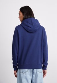 Haut à capuche bleu marine avec cordon de serrage, en tissu doux, à manches longues et avec des poignets côtelés, associé à un jean en denim bleu clair.