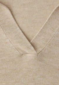 Tissu beige tricoté avec un détail d'encolure en V et une texture de points visible.