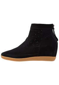 Bottine en daim noir avec design perforé, talon compensé et semelle en caoutchouc. Dotée d'une fermeture éclair latérale et d'une texture douce.