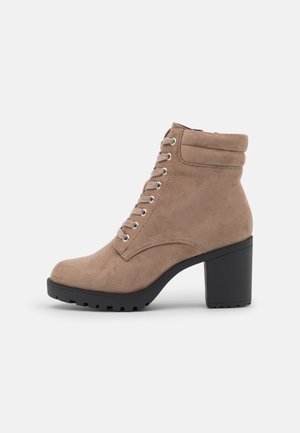 Bottine taupe en daim à lacets avec col rembourré, talon bloc noir épais et semelle crantée, montrée de profil sur fond blanc.