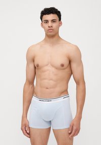 Shorts de boxe bleu clair avec une ceinture blanche comportant du texte noir, fabriqués en tissu doux, avec un design ajusté et des coutures minimales.