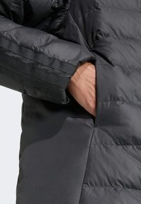 Czarna kurtka puchowa z teksturowaną powierzchnią, poziomym wzorem szycia oraz ukrytą kieszenią w lewym rękawie.