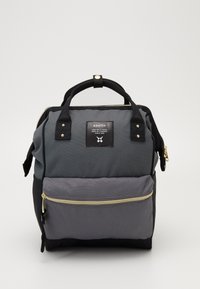 Kompaktowy, kwadratowy plecak z podwójnymi uchwytami u góry, przednią kieszenią na zamek oraz szaro-czarnym, kolorowym materiałem z naszywką z logo marki.