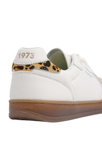 Sneaker bianco in pelle con dettagli in stampa leopardata sul tallone e suola in gomma marrone. Scritta dorata "1973" impressa sul tallone.