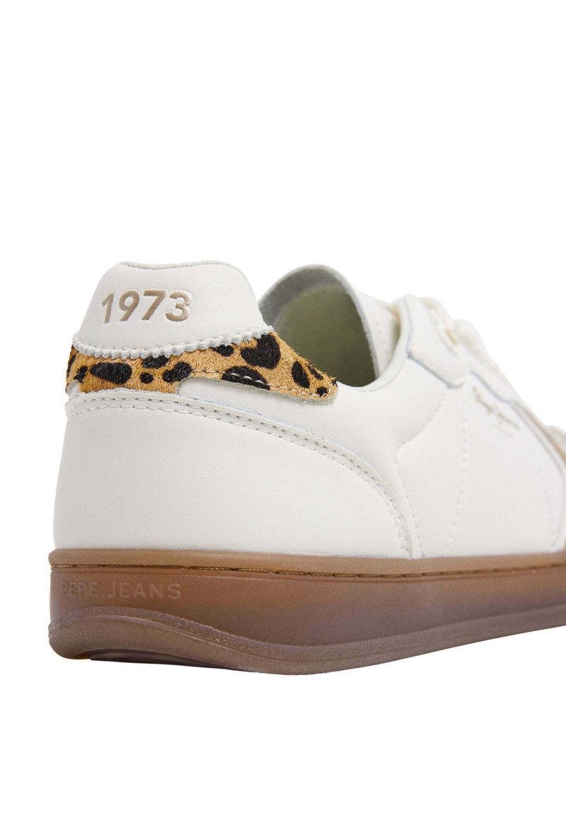 Zapatilla de cuero blanco con acentos de estampado de leopardo en el talón y suela de goma marrón. "1973" en dorado estampado en el talón.