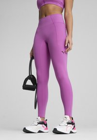 Legginguri roz ajustate cu un talie înaltă și detalii cu logo. Asortate cu pantofi sport negri și albi care au accente roz.