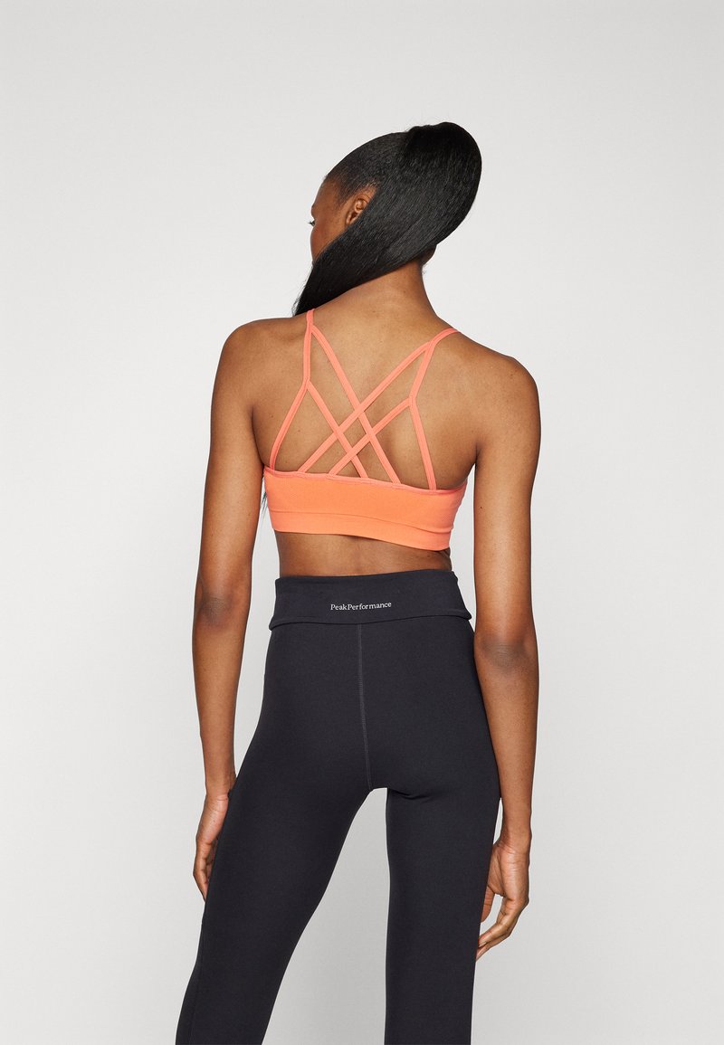 Rosa Sport-BH mit Kreuzträger-Design, kombiniert mit hochgeschnittenen schwarzen Leggings, die einen markenbezogenen Taillenbund und eine glatte Textur aufweisen.