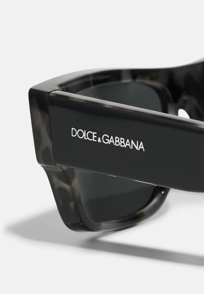 Ochelari de soare negri și țestoasă cu un design geometric, având lentile întunecate și logo-ul "Dolce & Gabbana" pe lateral.