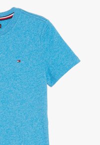 Jasnoniebieska melanżowa koszulka z krótkim rękawem, okrągłym dekoltem i małym logo w czerwonym, białym i niebieskim kolorze na lewej części klatki piersiowej.