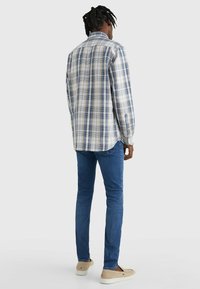 Camisa de cuadros en azul, beige y blanco, de manga larga, vista desde atrás. Combinada con vaqueros azules y zapatos de color claro. Tejido de algodón suave.