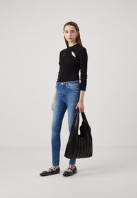Top negro de canalé con recortes, vaqueros ajustados azules, bolso plisado negro y bailarinas negras con lunares blancos y tachuelas.