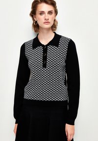 Schwarz-weißer Strickpullover mit Kragen, der ein geometrisches Muster, eine Knopfleiste und lange Ärmel aufweist. Glatte Textur.