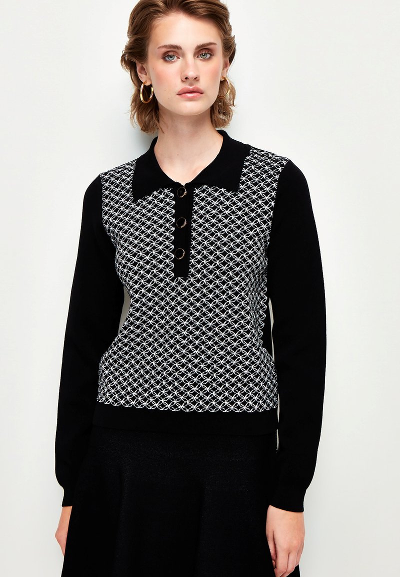 Schwarz-weißer Strickpullover mit Kragen, der ein geometrisches Muster, eine Knopfleiste und lange Ärmel aufweist. Glatte Textur.
