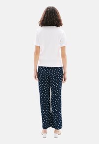 Witte top met korte mouwen in combinatie met marineblauwe broek met stippen, voorzien van een ontspannen pasvorm en een gladde textuur. Schoenen hebben dikke witte hakken.
