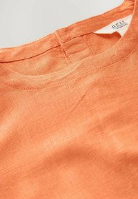 Orange linen fabric with a textured finish, featuring a rounded neckline and a stitched edge at the collar. Label visible.