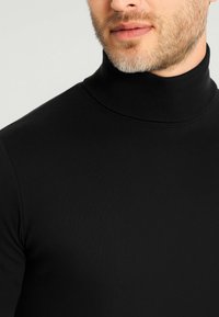 Maglione nero a collo alto realizzato in tessuto a coste, caratterizzato da un collo alto e da un design aderente che si adatta al corpo.