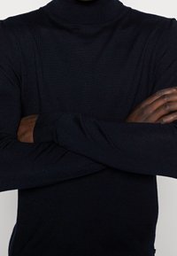 Pull à col roulé noir avec texture côtelée, coupe ajustée et manches longues, doté de poignets serrés et d'une finition sans coutures.