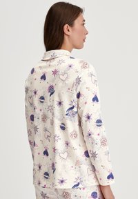 Lange mouwen pyjama shirt in crème, met een speelse print van harten, sterren en planeten in paars, roze en blauw. Zachte stof, relaxte pasvorm.