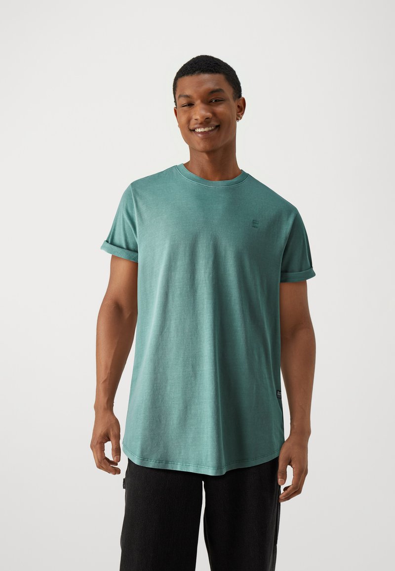 Rövid ujjú, türkiz t-shirt, puha anyagból, kerek nyakkivágással és felgöngyölt ujjal. Diszkrét logó részlet a mellrészen.