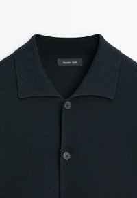 Navy polo shirt with a textured, knitted fabric. Features a classic collar and two black, four-hole buttons at the front. Logo tag visible.