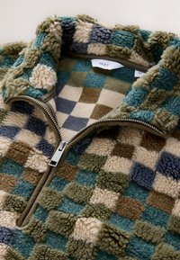 Mjukt rutig fleecejacka med en silverfärgad dragkedja och hög krage i nyanser av blått, grönt, brunt och beige.