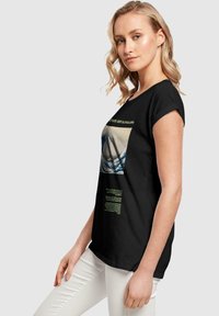 Camiseta de algodón negra con un gráfico frontal de una ola, acentuada con texto verde. La camiseta tiene un corte relajado y mangas cortas.