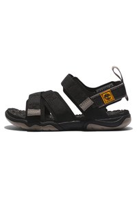 Svart sandal med justerbara remmar, texturerad sula och en vadderad fotbädd. Har en gul logotags på sidan och en ögla för dragning.