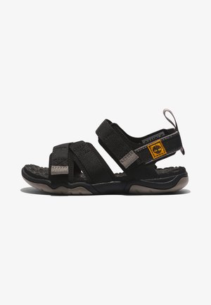 Svart sandal med justerbara remmar, texturerad sula och en vadderad fotbädd. Har en gul logotags på sidan och en ögla för dragning.