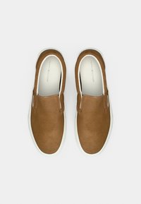 Ζευγάρι καφέ σουέτ αθλητικά παπούτσια slip-on με λευκές λαστιχένιες σόλες, φαίνονται από ψηλά, με την επωνυμία Tommy Hilfiger στο εσωτερικό.