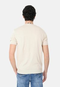 Pullover beige a maniche corte con polsini e orlo a coste, che mostra una texture liscia. Modello visto da dietro, indossando jeans blu.