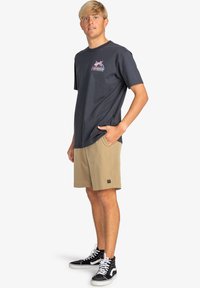 Camiseta negra de manga corta con un gráfico colorido, combinada con pantalones cortos de cuadros beige y zapatillas altas negras con cordones blancos.