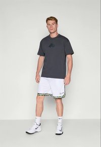 Herretøj til afslappede anledninger bestående af en mørkegrå T-shirt og hvide shorts med et farverigt mønster ved kanten, suppleret med hvide sportssko.