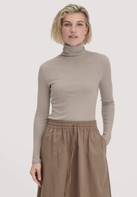 Beige Rollkragenoberteil aus weichem, elastischem Stoff mit langen Ärmeln. Kombiniert mit einem braunen Rock mit elastischem Bund.