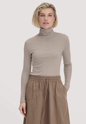 Beige coltrui gemaakt van zachte, rekbare stof met lange mouwen. Gecombineerd met een bruine rok met elastische taille.