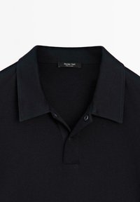 Černé polo tričko se standardním límečkem, dvouknoflíkovým zapínáním a hladkou texturou. Na štítku je nápis "Massimo Dutti." Vyrobeno z elastického materiálu.