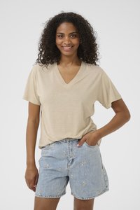 T-shirt beige à col en V en tissu doux, associé à un short en denim bleu clair avec broderies florales et coupe décontractée.