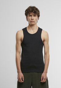 Schwarzes Baumwoll-Tanktop mit rundem Ausschnitt und breiten Trägern, mit einer schmalen Passform und glatter Textur. Kombiniert mit strukturierten grünen Shorts.