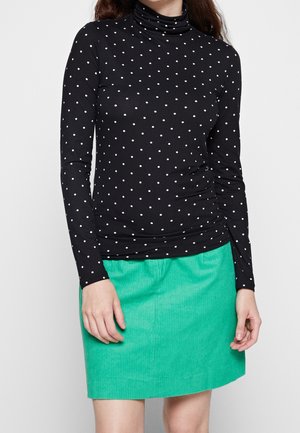 Schwarzer Rollkragenpullover mit weißen Polka-Dots, kombiniert mit einem grünen Cordrock. Lange Ärmel, glatte Textur, figurbetontes Design.