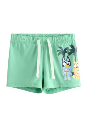 Costume da bagno verde chiaro con coulisse bianche raffigurante cani dei cartoni animati che tengono coni gelato e palme sulla gamba destra.