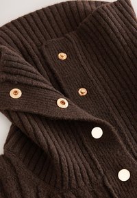 Cardigan marrone a costine in maglia con bottoni dorati e dettagli testurizzati. Il materiale appare morbido e spesso, garantendo calore e comfort.
