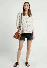 Blusa branca com padrões coloridos, mangas três quartos, combinada com calções escuros. Saco de ombro castanho e sandálias em slide castanhas.