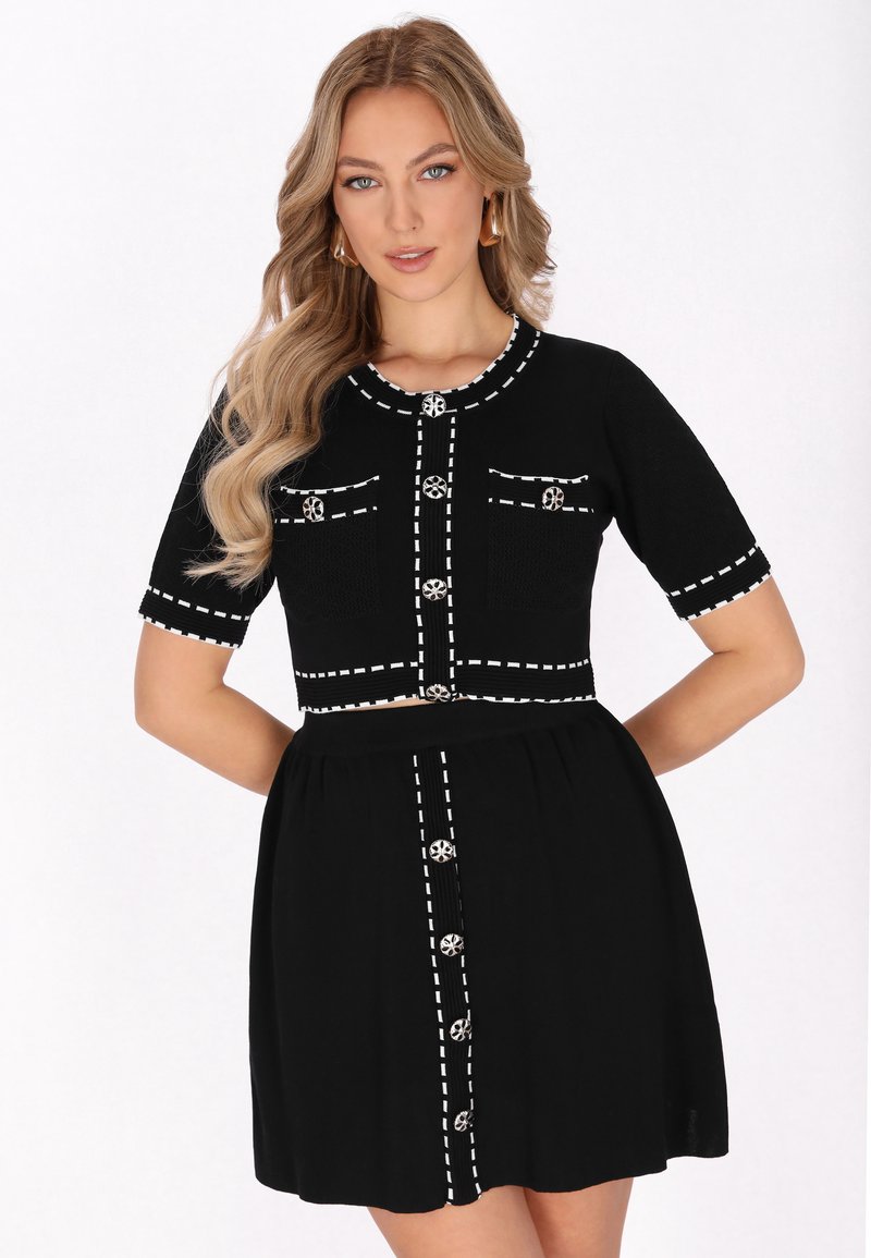 Schwarzes Kleid mit einem figurbetonten strukturierten Oberteil, kurzen Ärmeln und einem ausgestellten Rock. Mit weißen Steppnähten und dekorativen Knöpfen erhältlich.