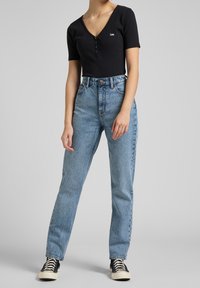 Sort ribbet kortærmet top med knapper, parret med høj talje blå denim jeans. Jeansene har en klassisk lige ben silhuet.
